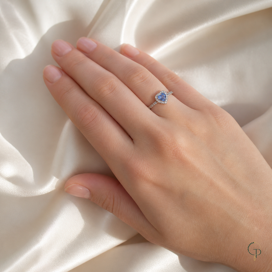Silver-color blue heart halo ring worn correctly on an anonymous hand over ivory silk