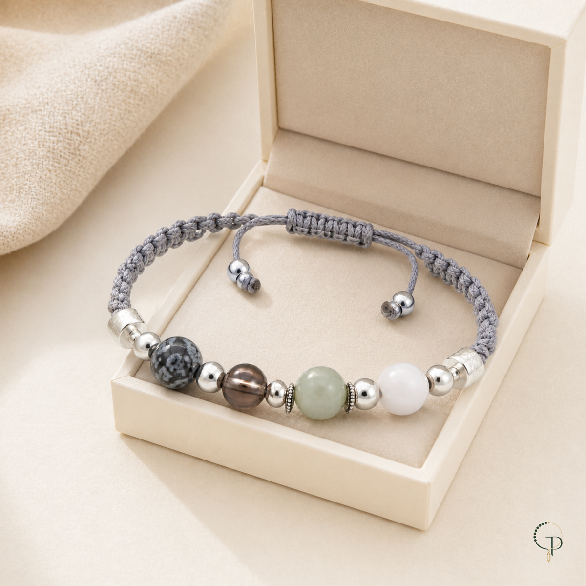 Mixed-bead gray braided cord bracelet displayed in an unbranded ivory jewelry box