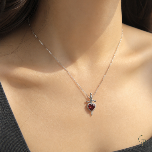 Red heart sword pendant necklace worn at the collarbone with a dark square-neck top