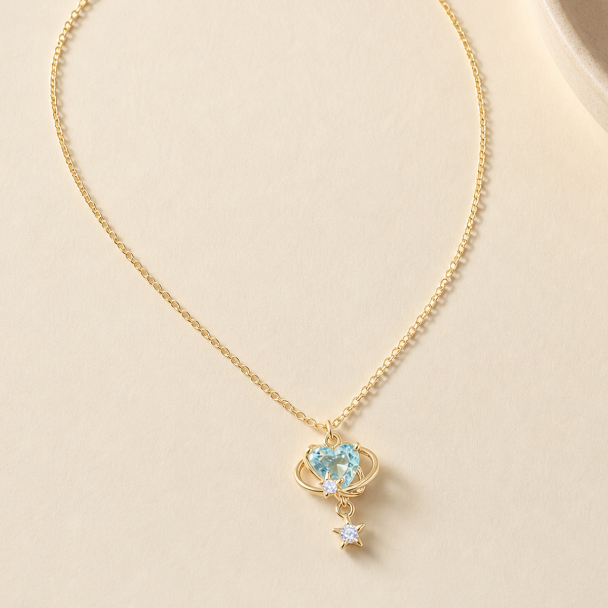 Aqua orbit star drop necklace laid on a softly lit ivory surface