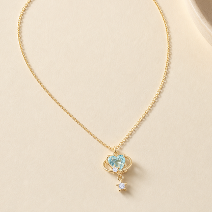 Aqua orbit star drop necklace laid on a softly lit ivory surface
