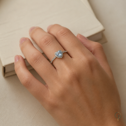 Blue heart halo ring worn correctly on an anonymous hand beside an ivory book