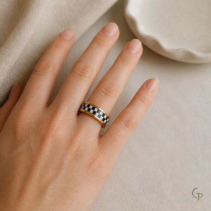 Gold-color checkerboard spinner ring worn on an anonymous hand beside a cream ceramic dish