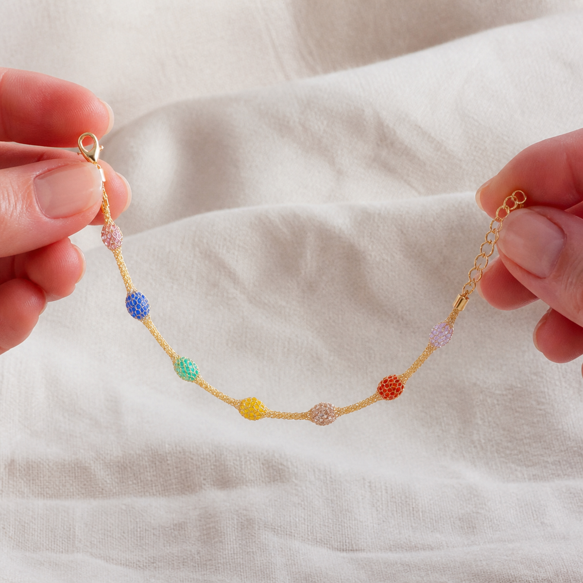 Rainbow mesh bead bracelet held in two hands to show scale and construction