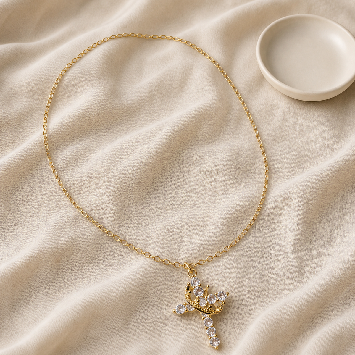 Crown cross necklace styled beside an ivory ceramic dish