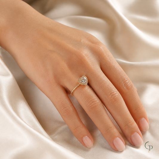 Gold-color heart halo ring worn on an anonymous hand over ivory silk