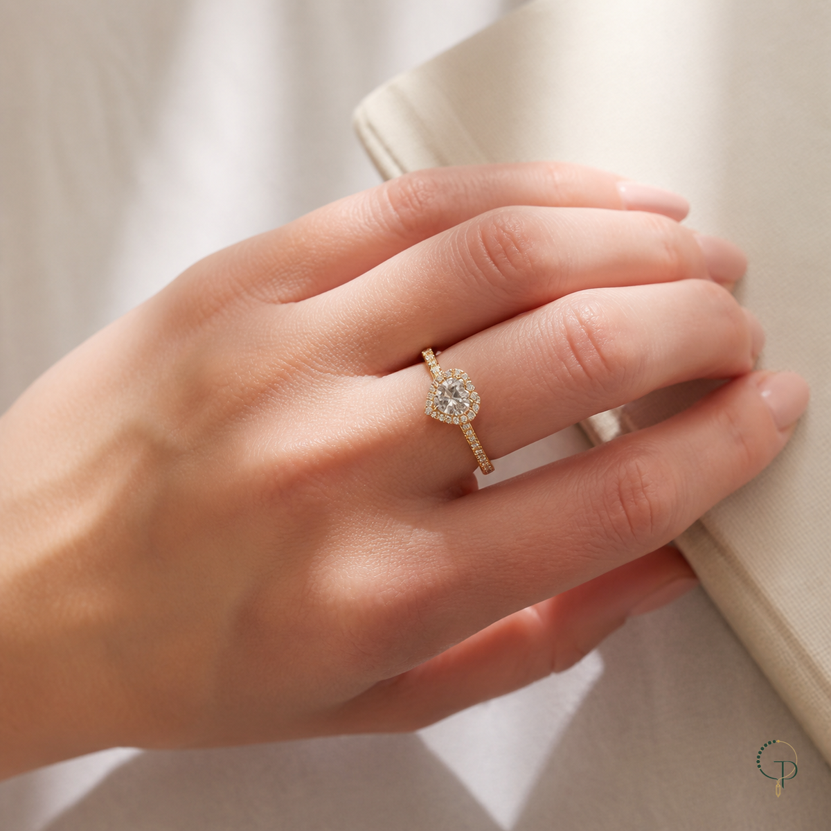 Gold-color heart halo ring worn beside an ivory linen book