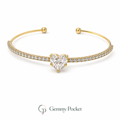 Gold-color open cuff bracelet with a clear heart-shaped center stone on a white background.