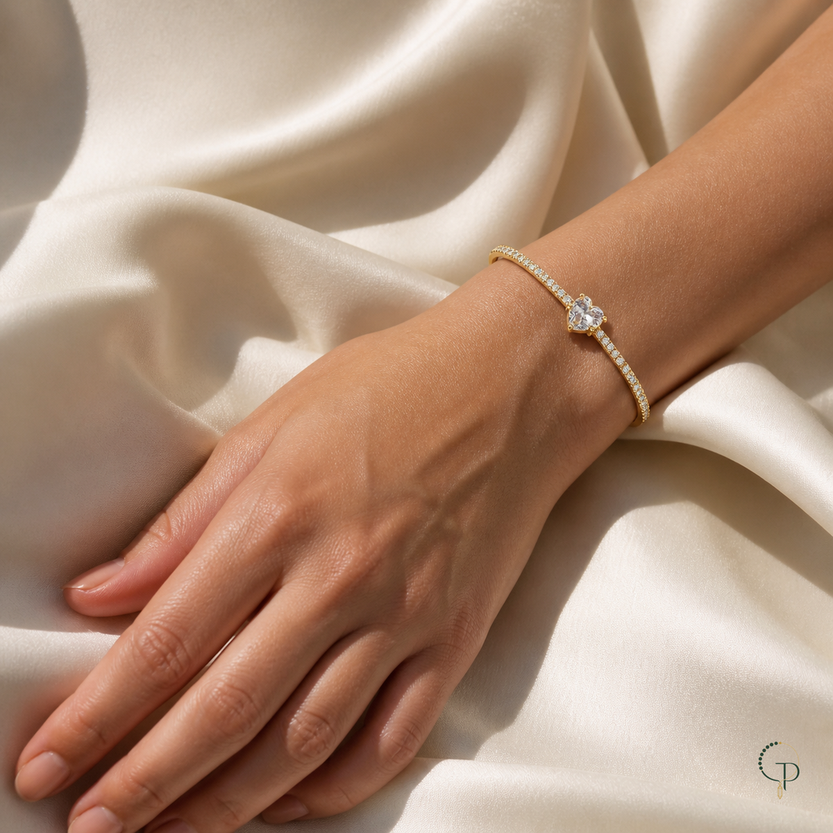 Gold-color heart cuff bracelet styled on a relaxed wrist and hand over ivory fabric.