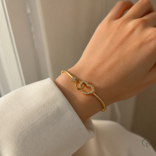 Interlocking two-heart gold-color bracelet worn around an anonymous wrist