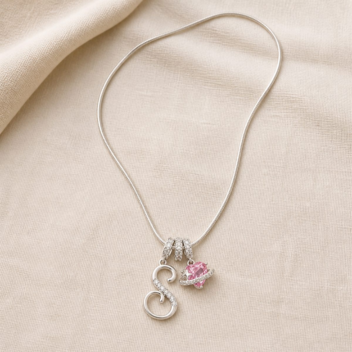 Full dual-charm snake chain necklace laid flat on ivory linen
