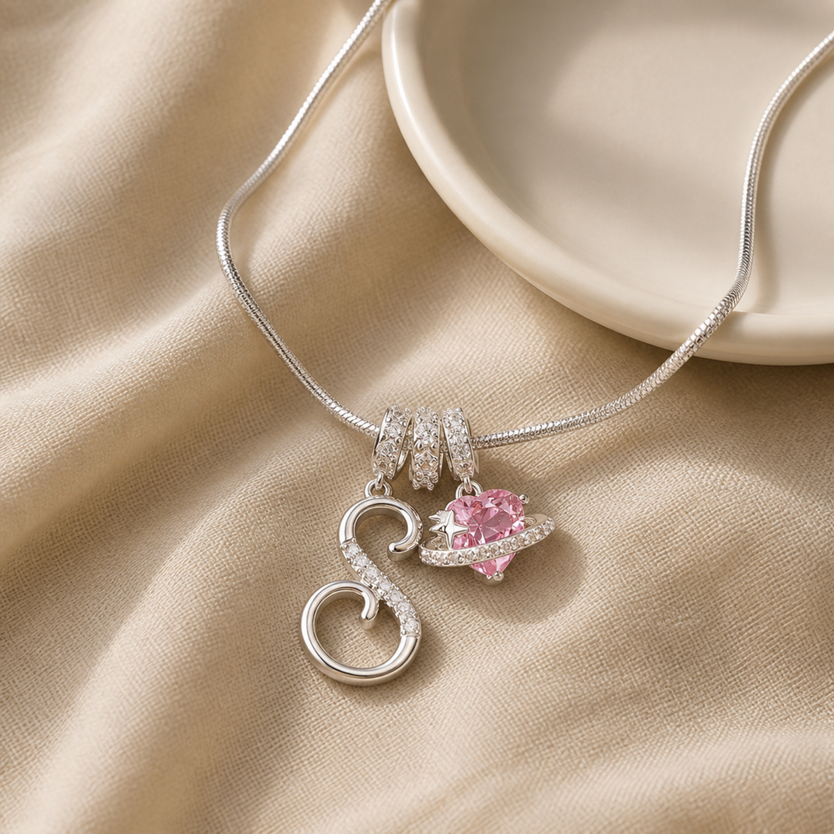 Pink planet and S charm necklace beside an ivory ceramic dish