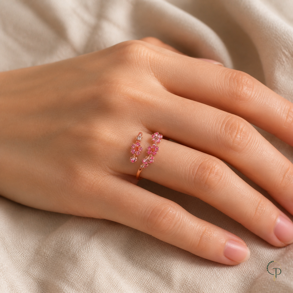 Pink blossom bypass ring worn at natural scale on a hand over cream linen