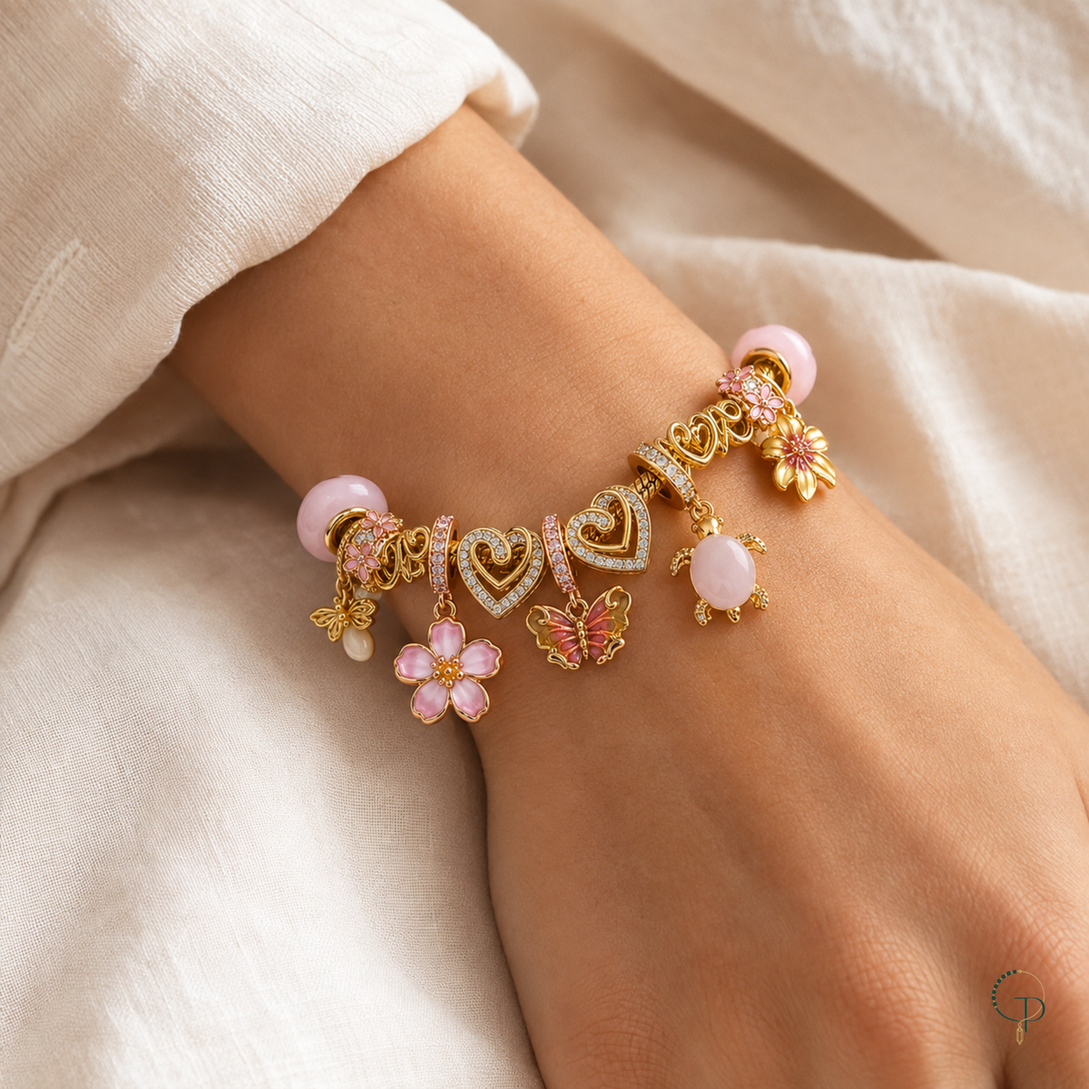 Pink and gold-color flower, butterfly and turtle charm bracelet worn on a wrist against ivory linen