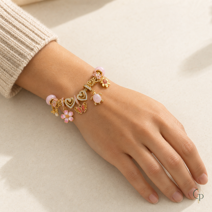 Gold-color and pink charm bracelet shown on a relaxed hand with a cream knit sleeve