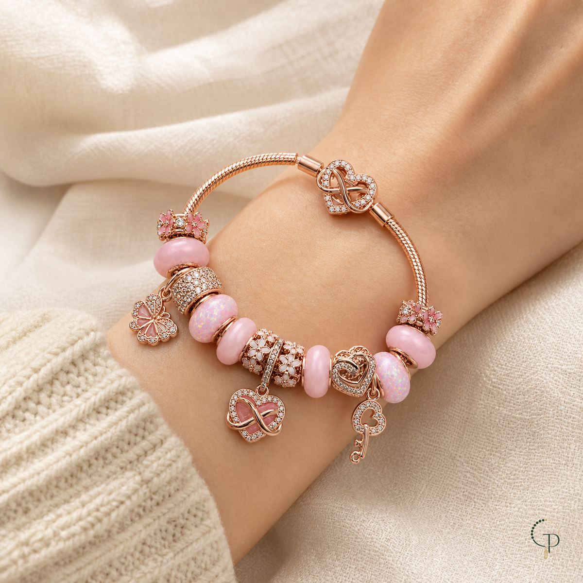 Pink infinity charm bracelet worn on a wrist beside a cream knit cuff