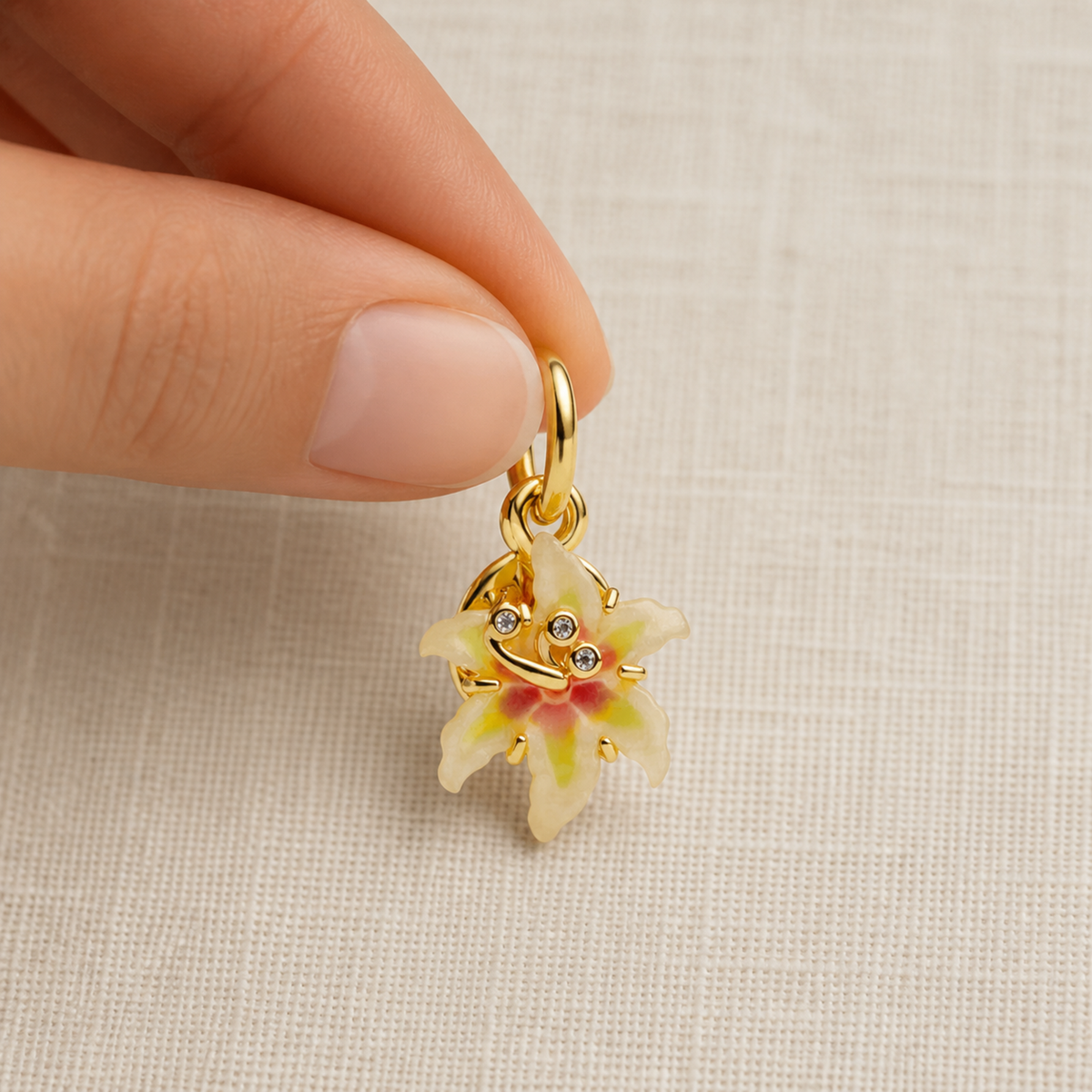 Enamel flower pendant charm held between two fingers to show scale