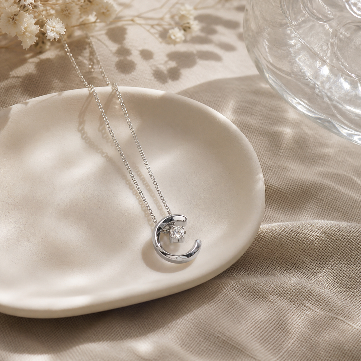 Silver crescent moon crystal necklace styled on an ivory ceramic dish
