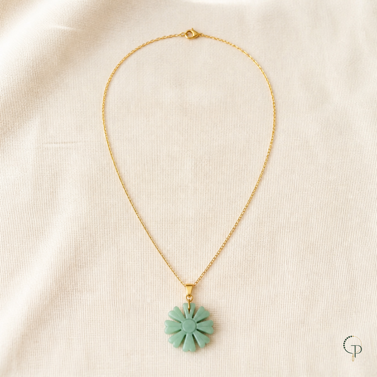Gold-color chain and seafoam sunburst pendant arranged on ivory linen