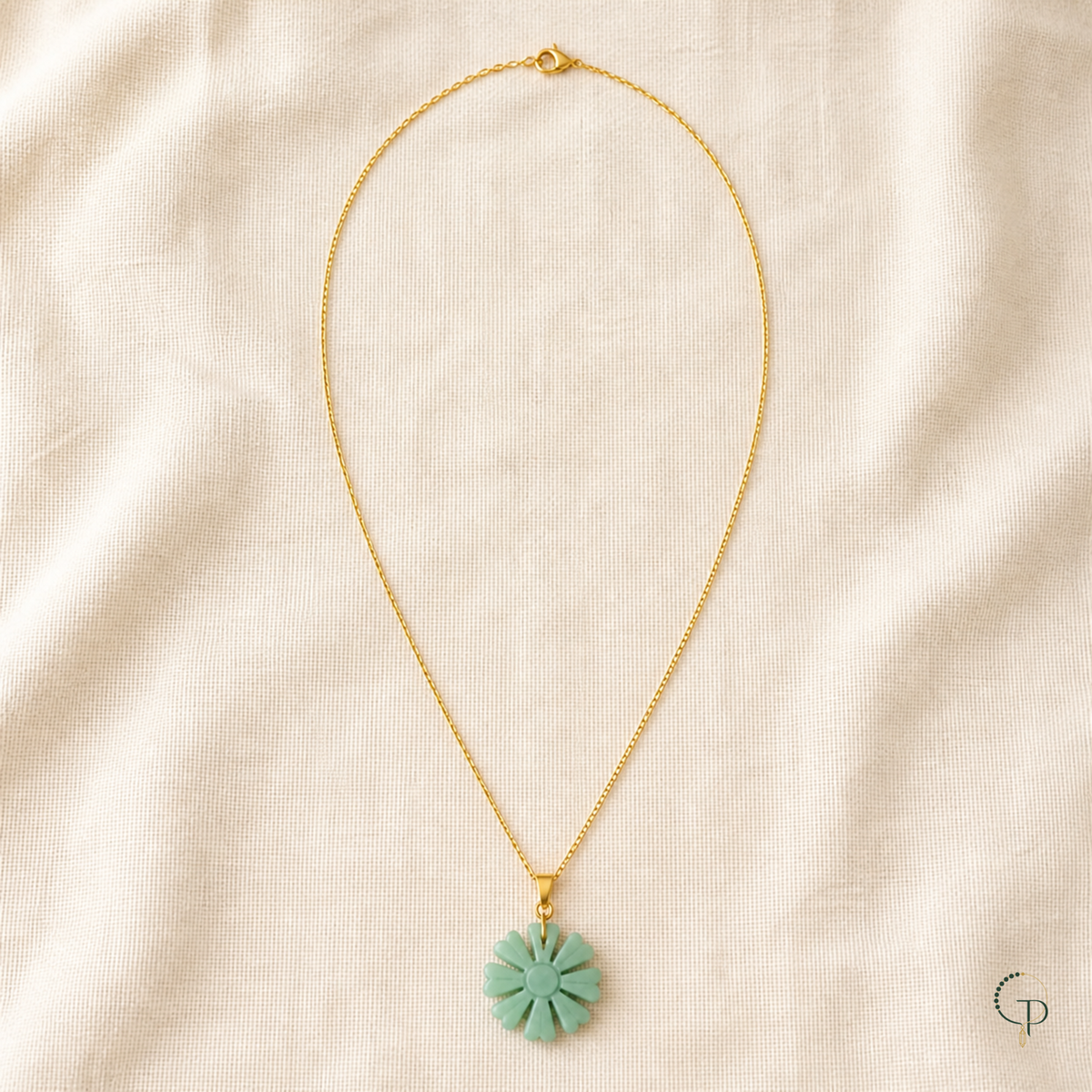 Complete gold-color chain with clasp and seafoam sunburst pendant arranged on ivory linen