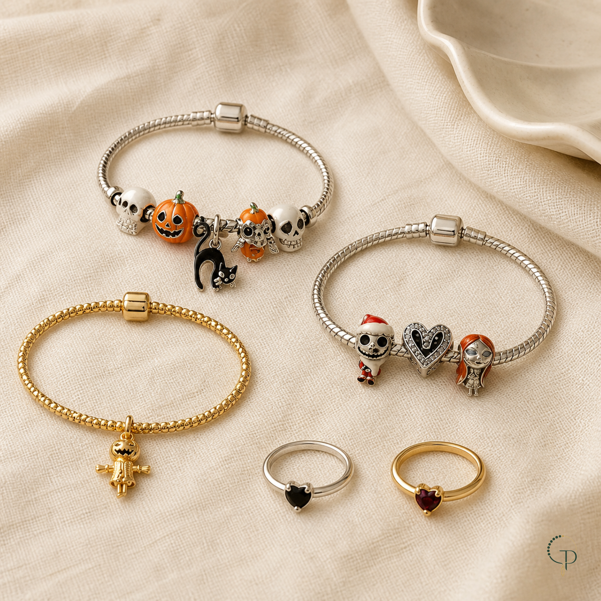 Three charm bracelets and two heart rings arranged on warm ivory linen