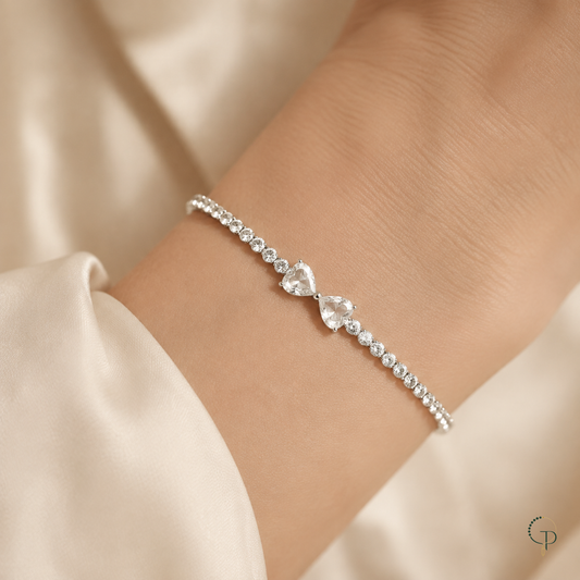 Silver-color twin heart bow tennis bracelet worn on a wrist with an ivory sleeve