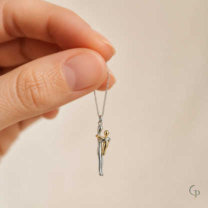 Hand holding the fine chain above the two-tone embrace figure pendant