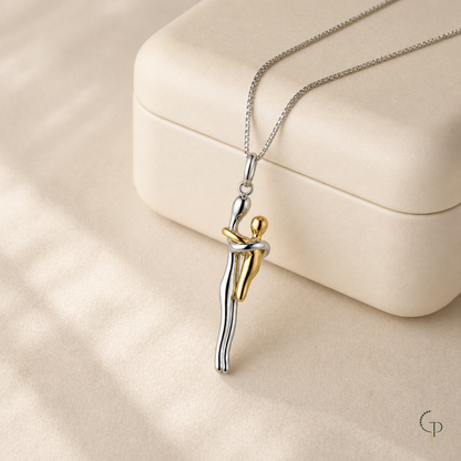 Two-tone embrace figure pendant necklace displayed in a plain ivory jewelry box