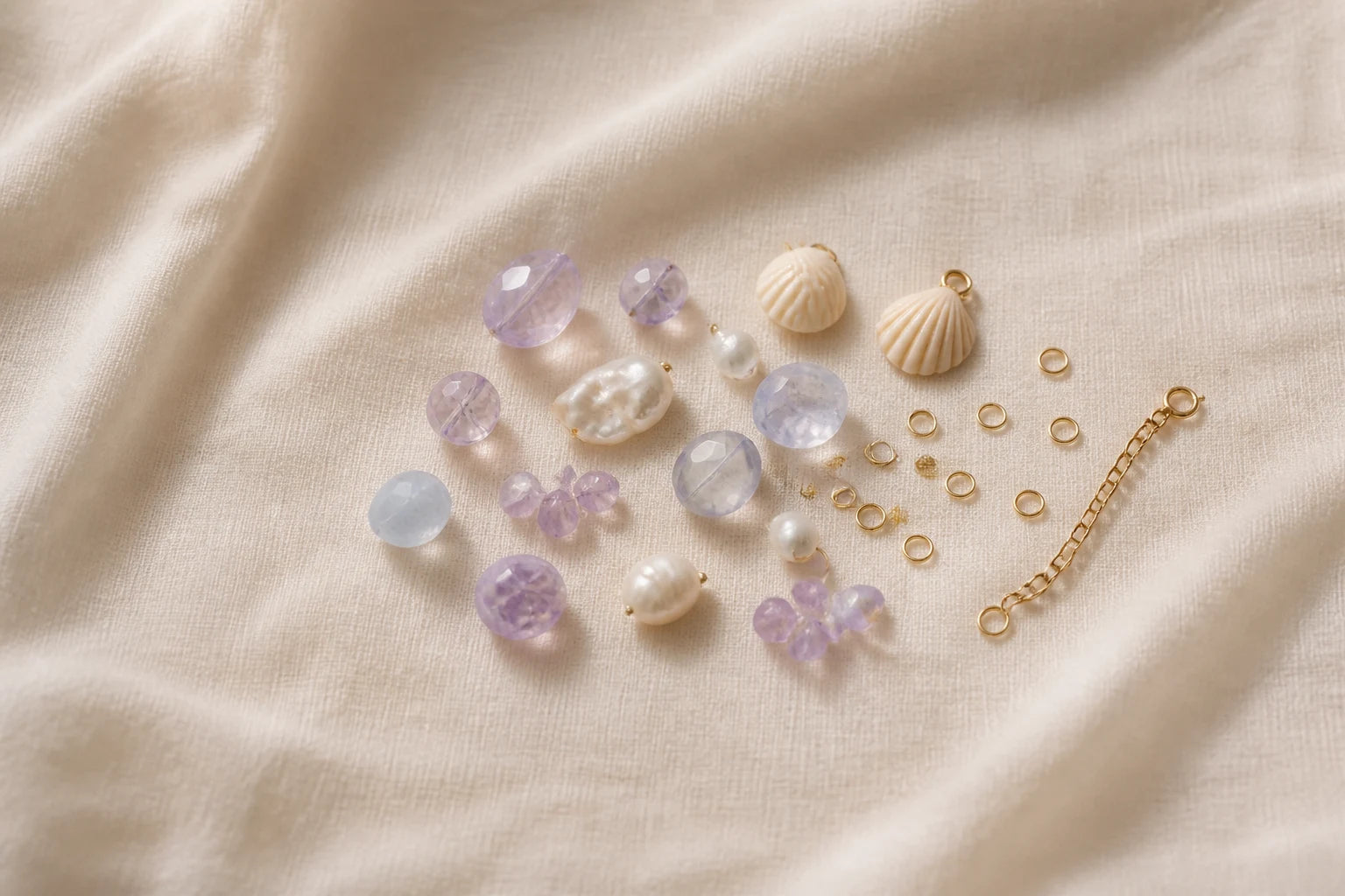 Gemmy Pocket lavender crystals, pearls, shell charms and gold-tone findings arranged on ivory linen
